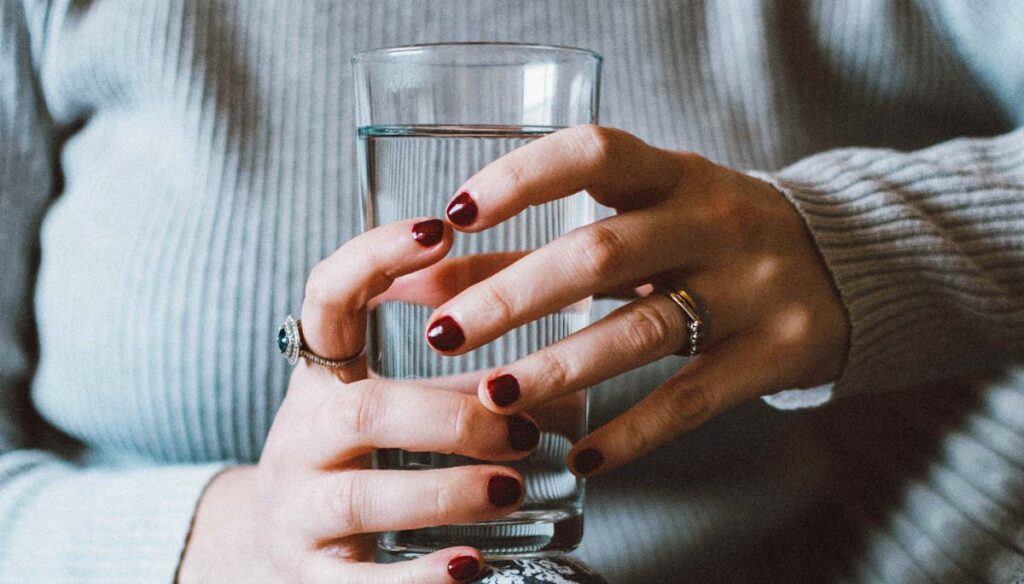 Woman holding glass of water since hydration rules before surgery were updated.