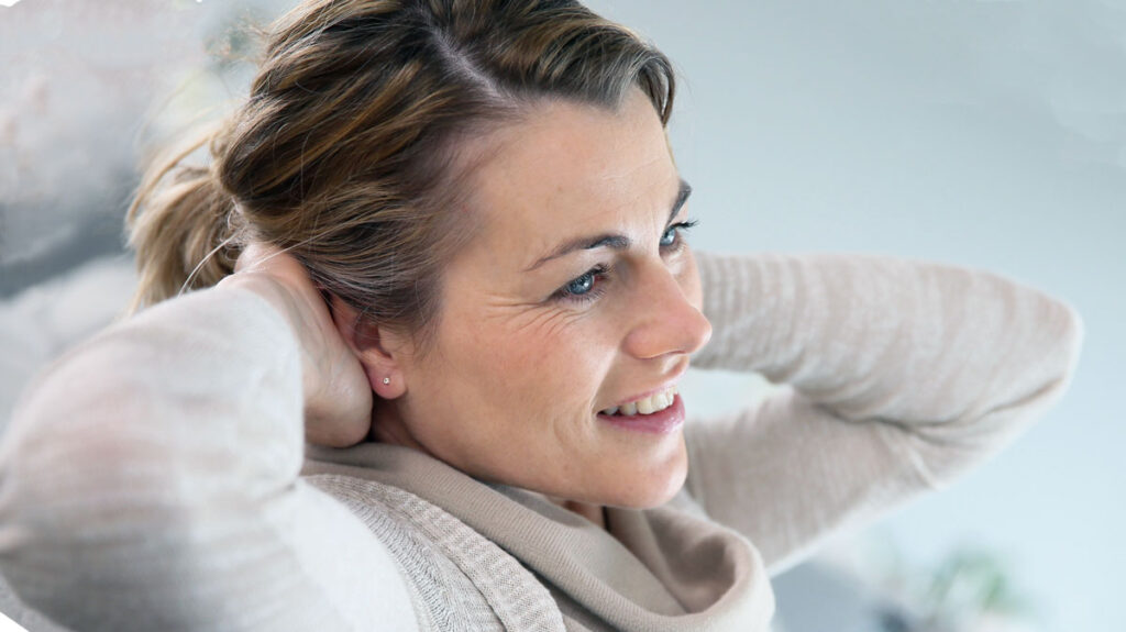 Middle-aged woman holding hands behind her neck- in a good age for a neck lift consultation.