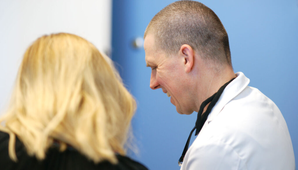 Facelift Consultation with doctor Mark Domanski- patient asking questions during consultation. Dr Domanski smiling to the patient who's long hair are visible.